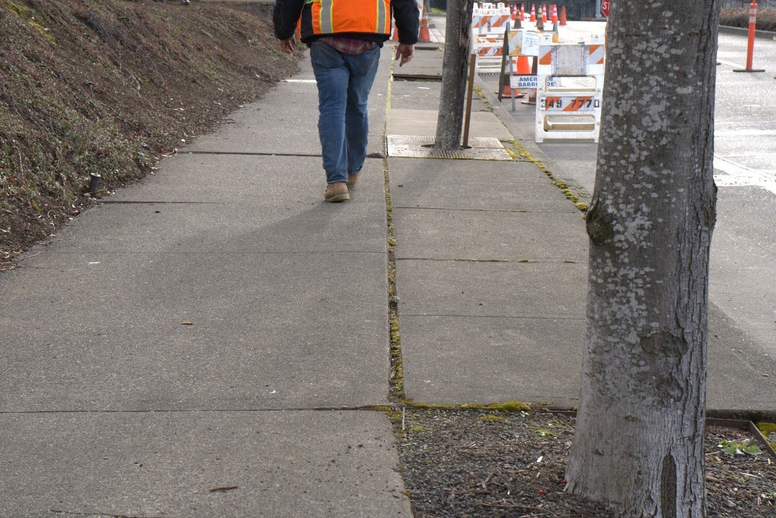 A man in an orange vest is walking down a sidewalk.