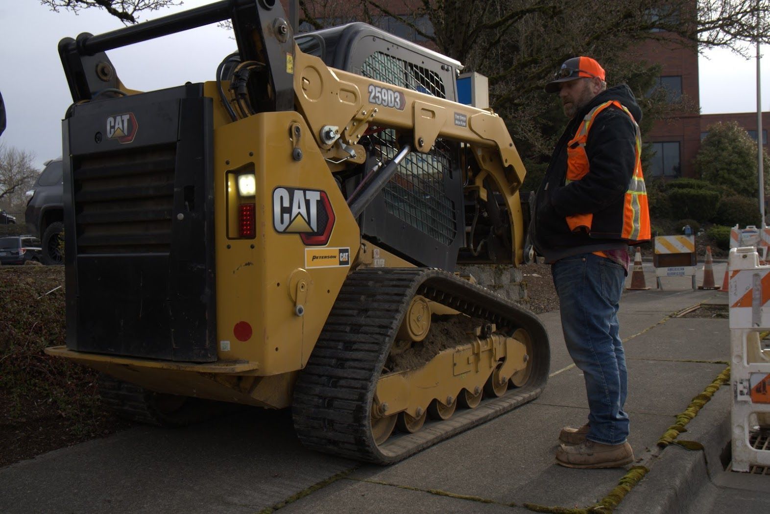 A man in an orange vest is standing next to a cat bulldozer.
