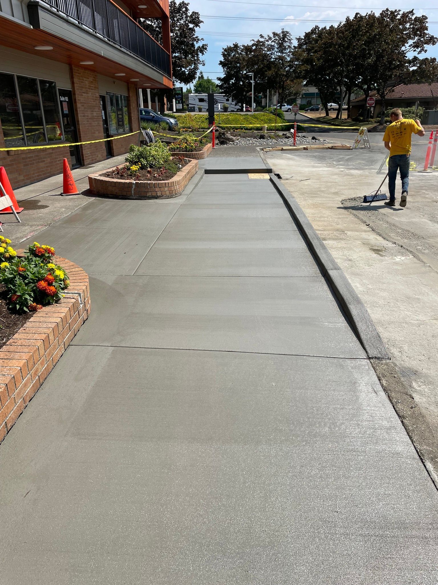A man is spreading concrete on a sidewalk in front of a building.