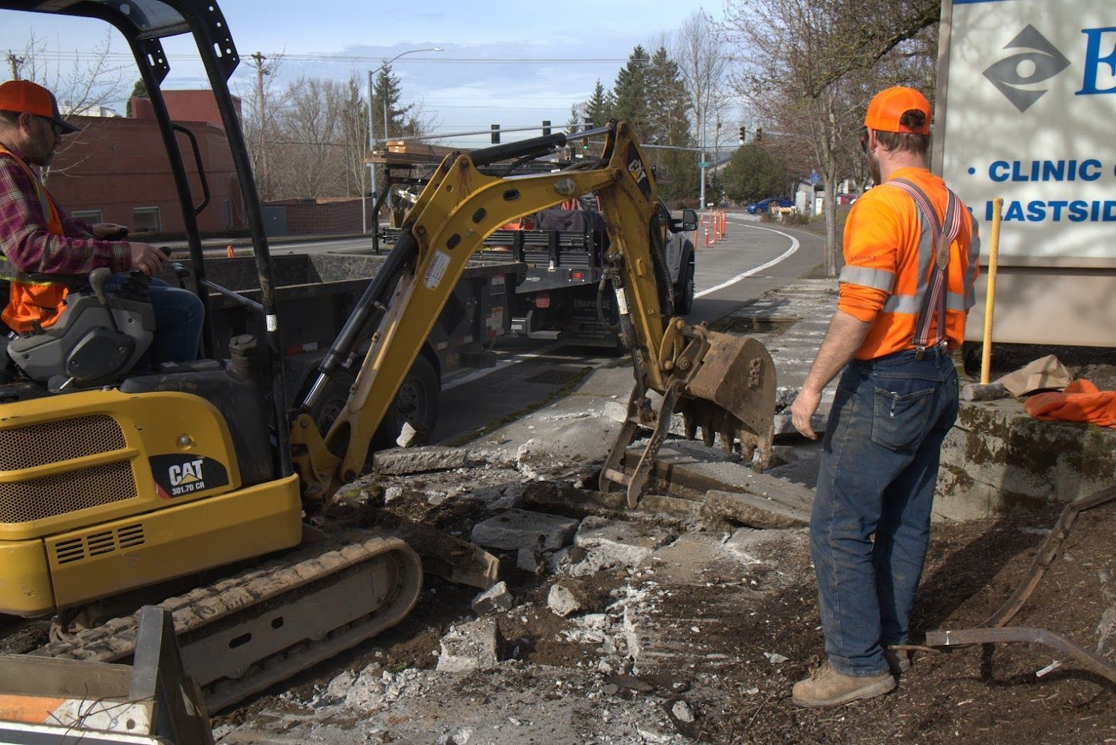 A man in an orange vest is standing in front of an excavator.