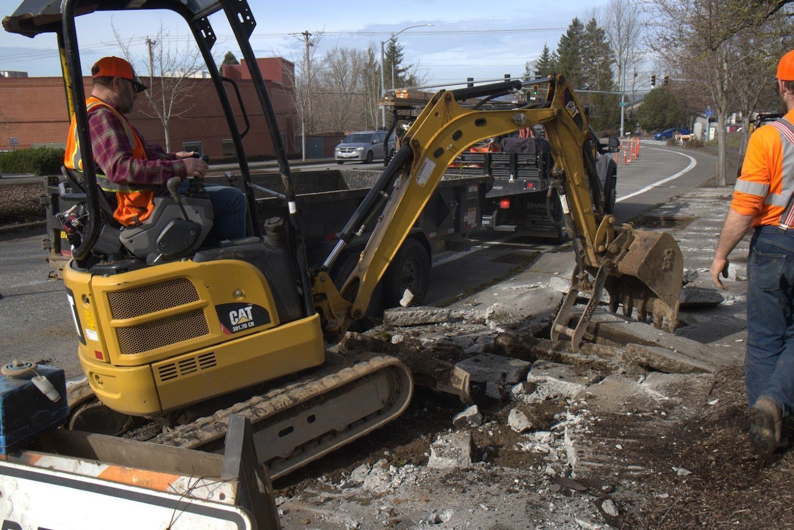 A man is driving a yellow cat excavator on a street.