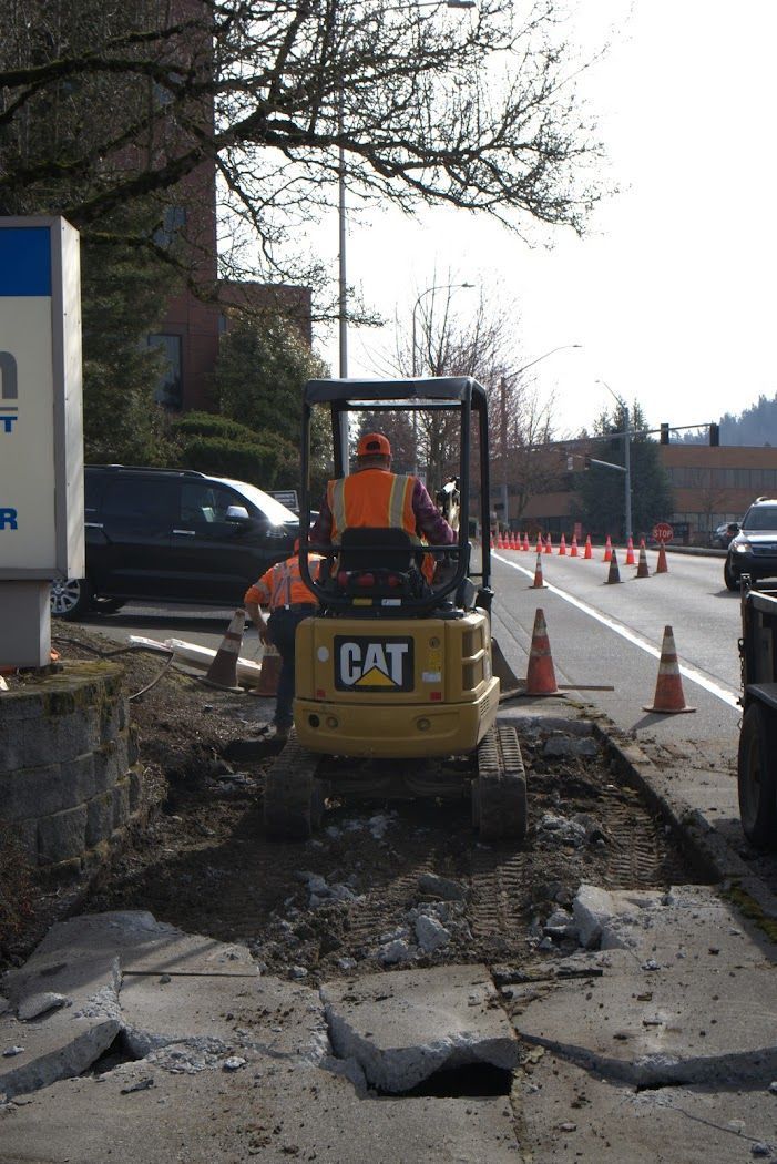 A man is driving a cat excavator on the side of the road