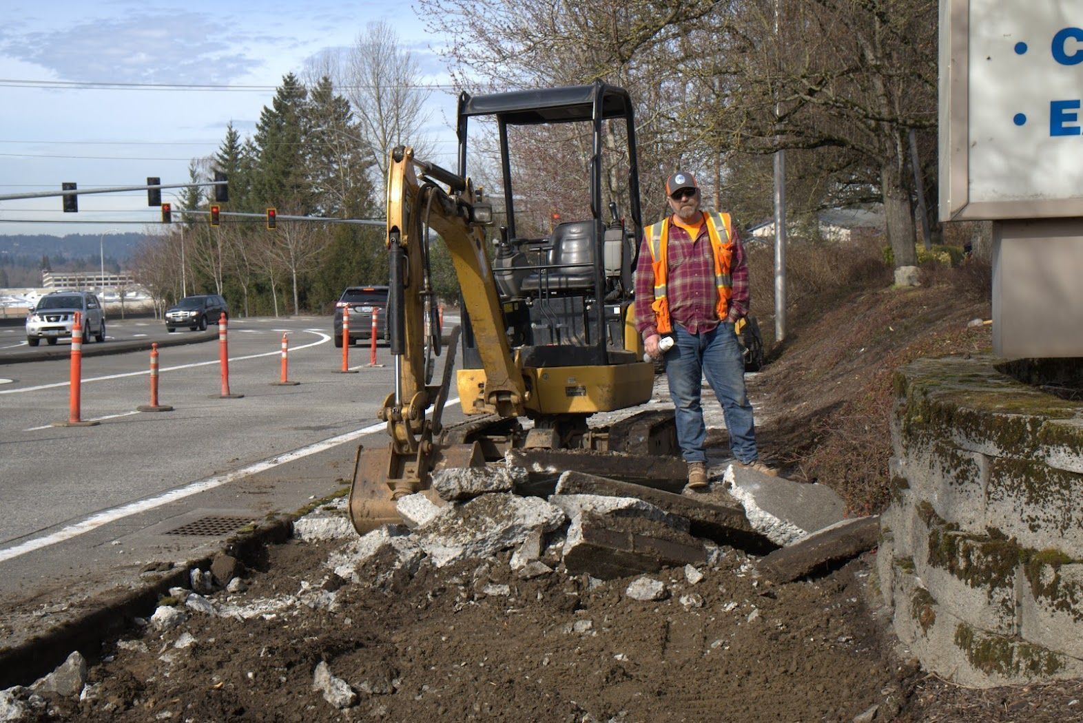 A man in an orange vest is standing in front of an excavator