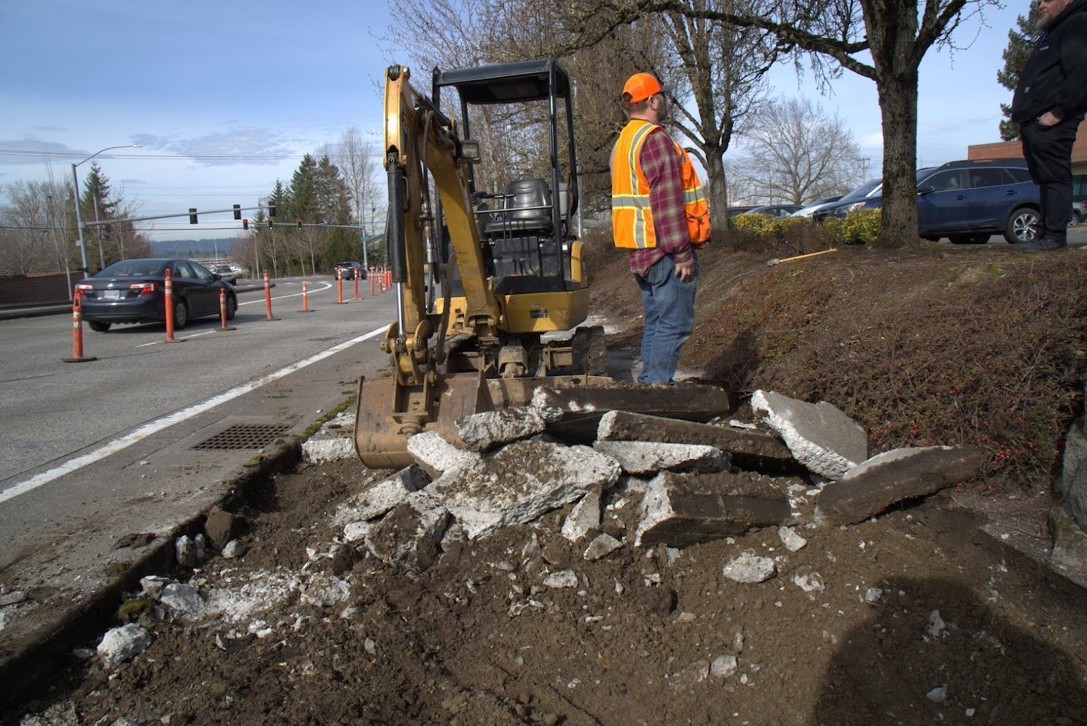 A man in an orange vest is standing next to an excavator.