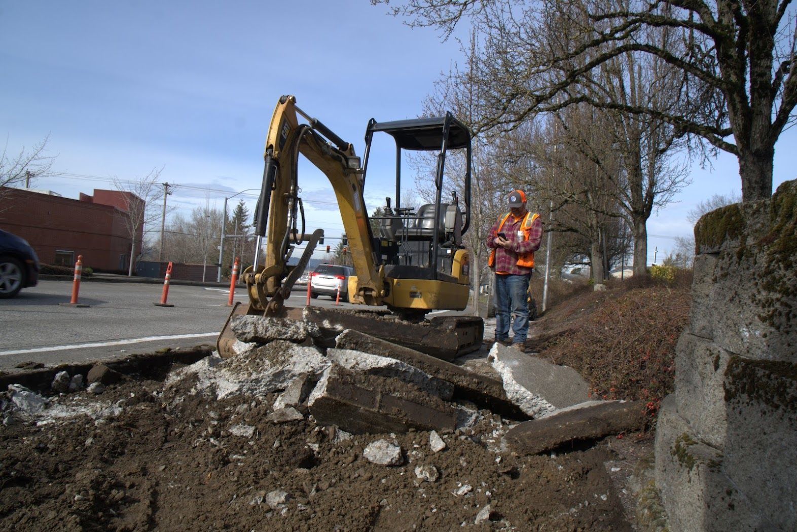 A man is standing next to a small excavator in a parking lot.