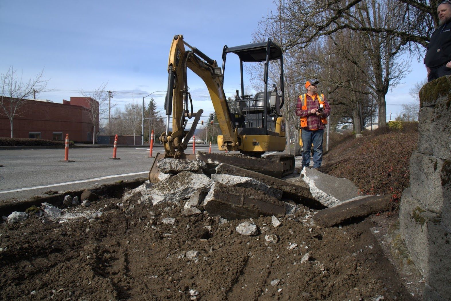 A man is standing in front of a yellow excavator.