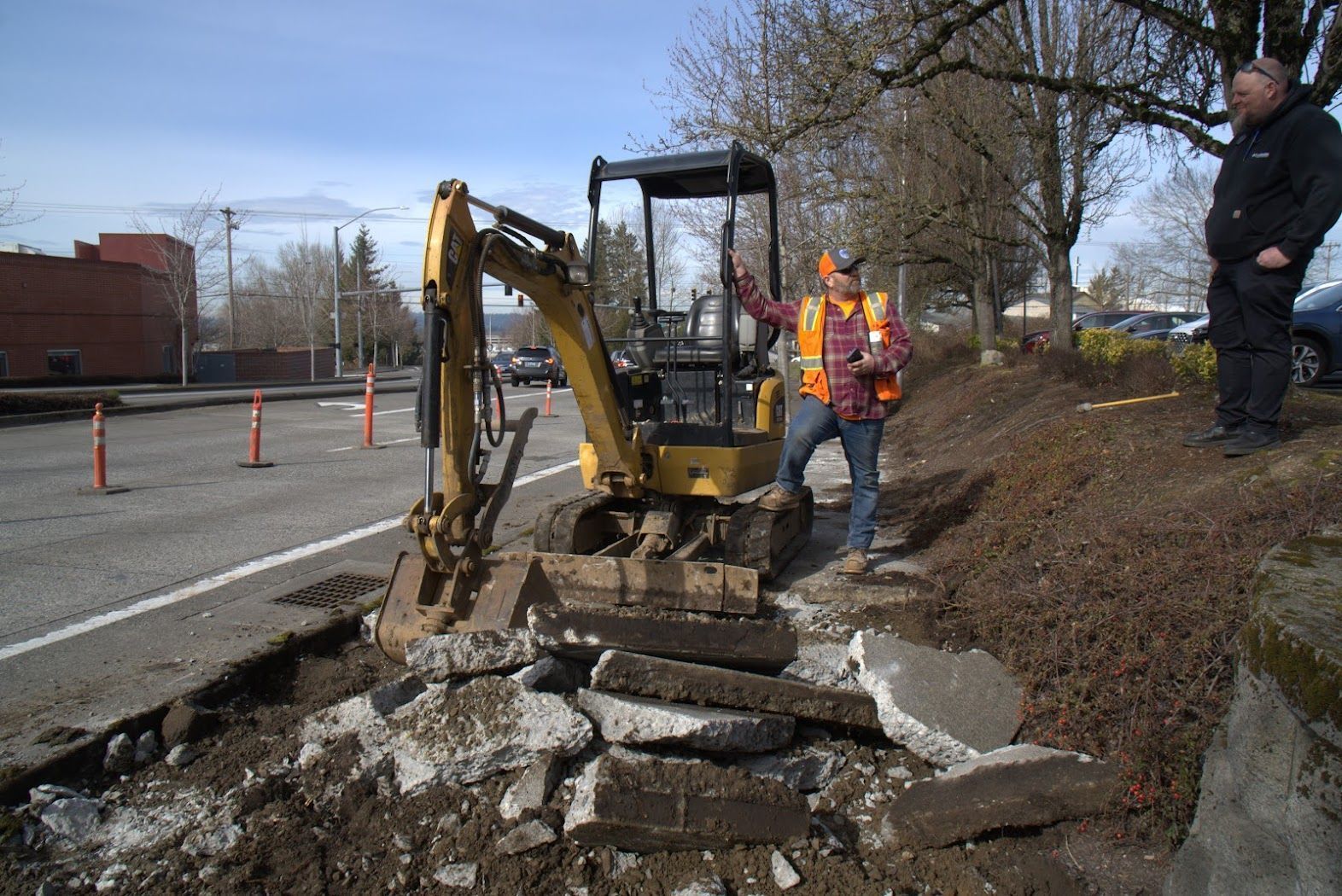 A man is standing next to a small yellow excavator.