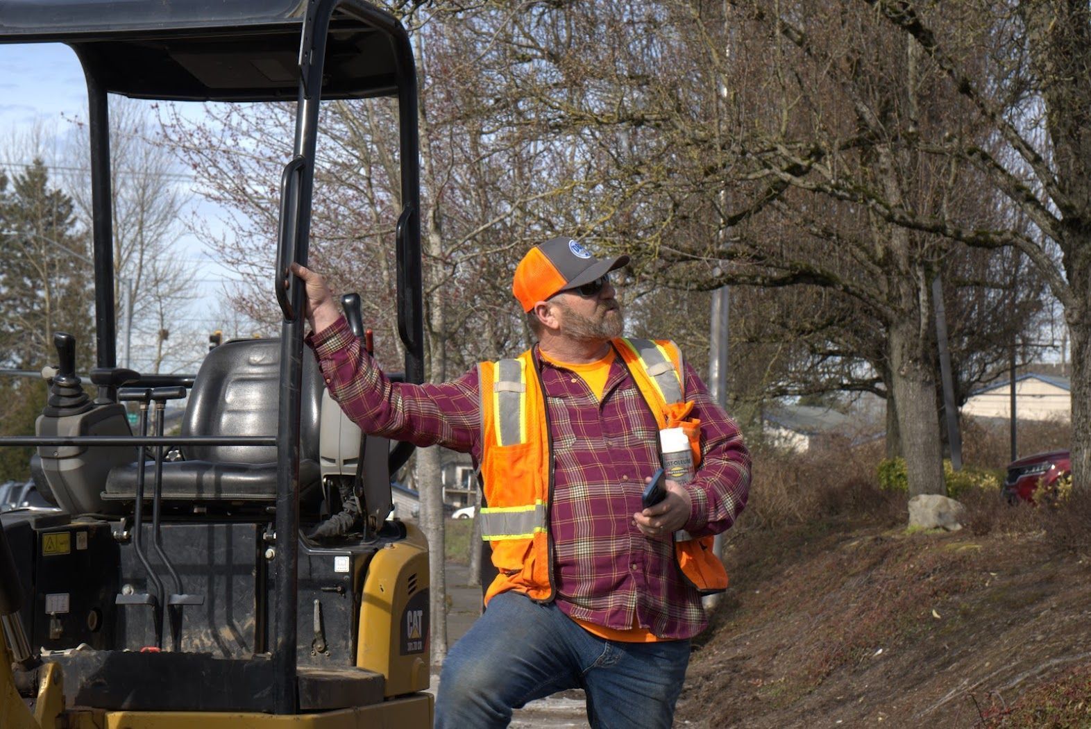 A man in a safety vest is standing next to a small excavator.