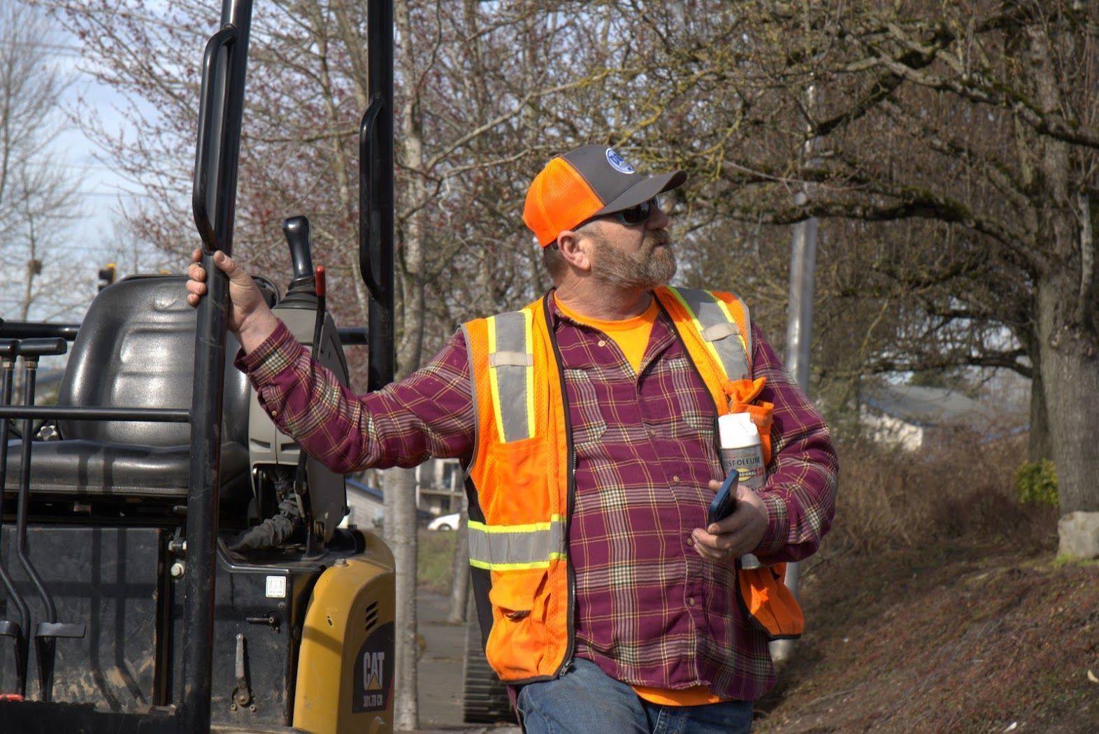 A man in an orange vest is standing next to a forklift.