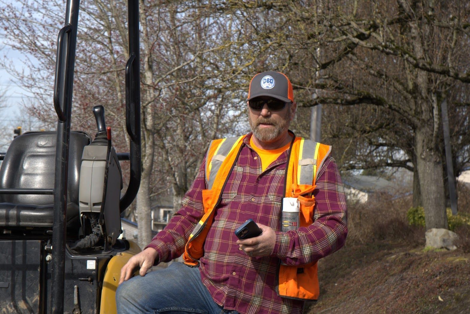 A man wearing a safety vest and sunglasses is sitting on a bulldozer.