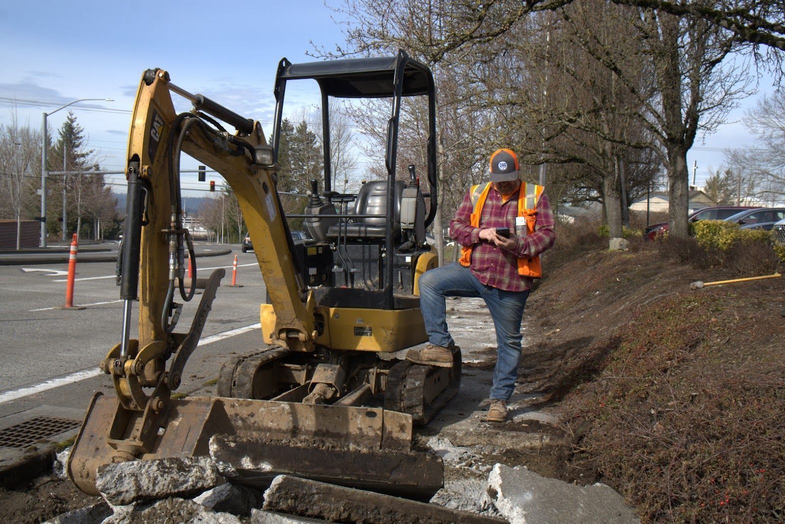 A construction worker is standing next to a small excavator.