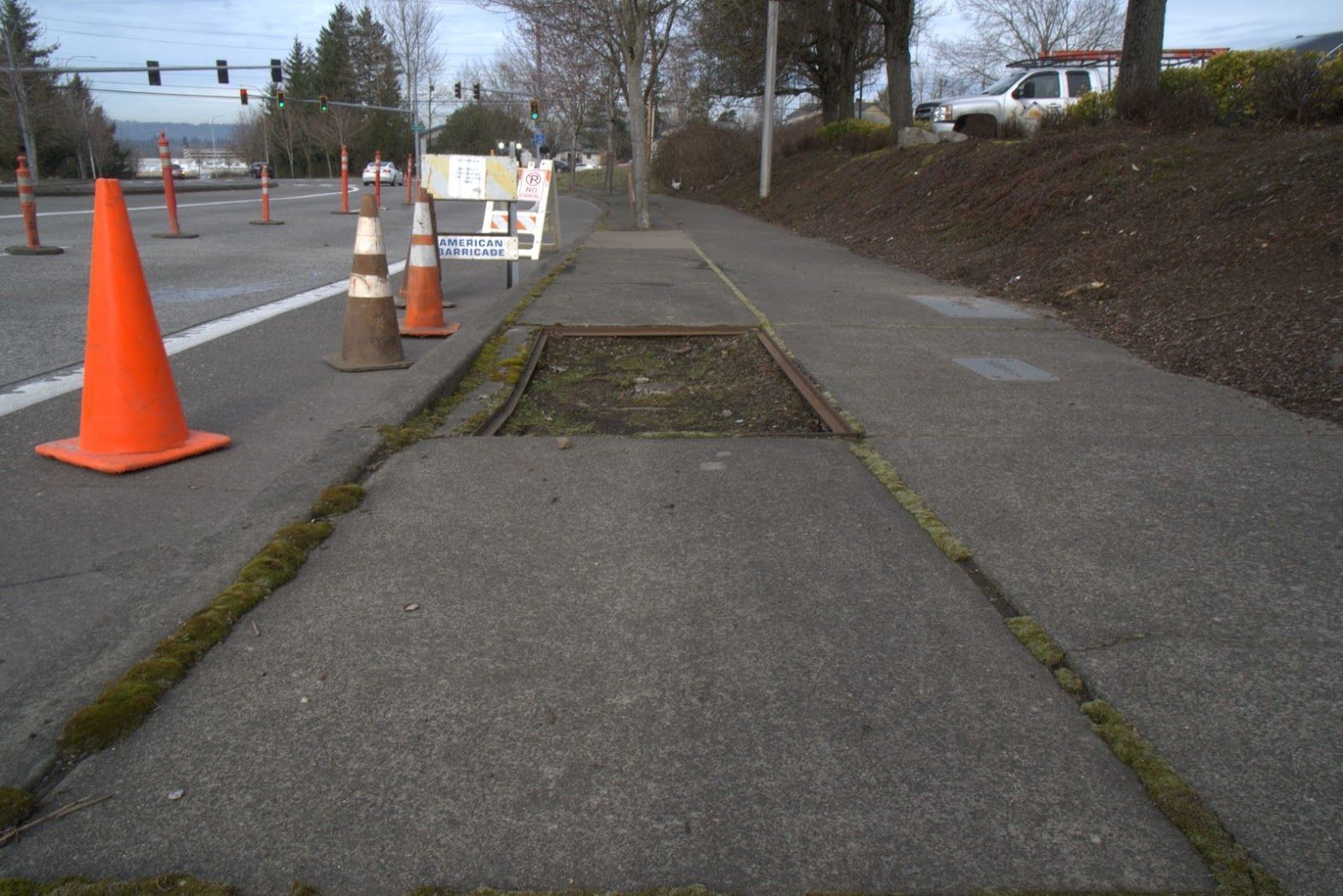 A sidewalk with a hole in it and orange cones on it