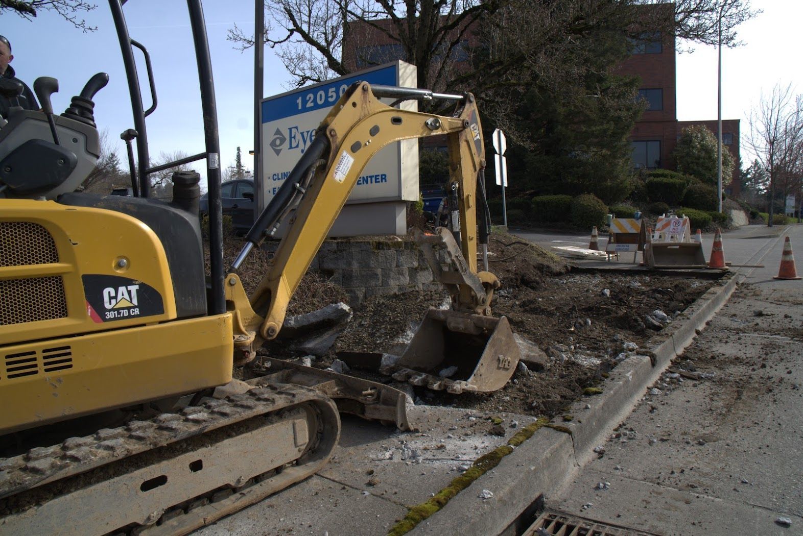 A cat excavator is digging a hole on the side of the road