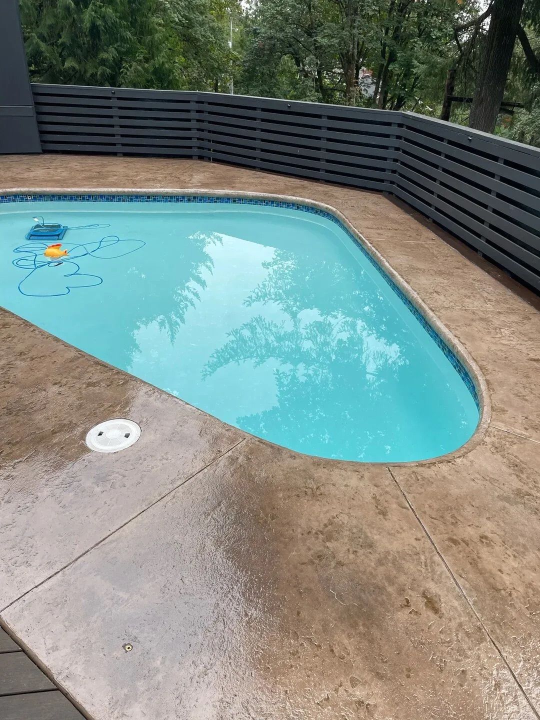 A swimming pool with a fence around it and trees in the background.