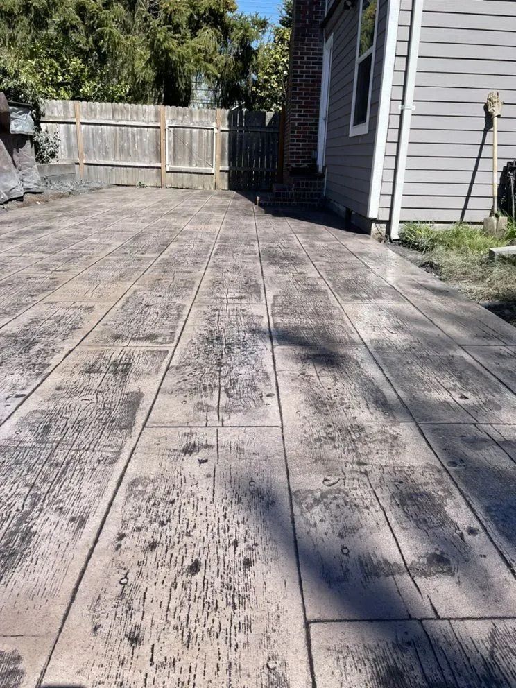 A concrete walkway leading to a house with a wooden fence in the background.