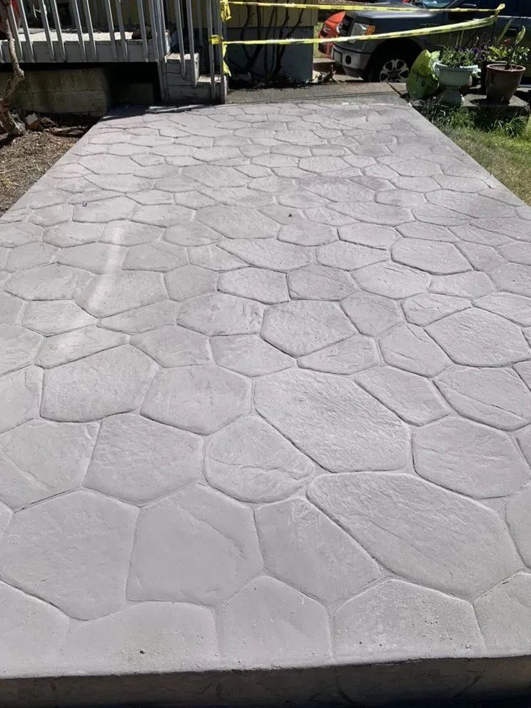 A concrete walkway with a geometric pattern is being built in front of a house.