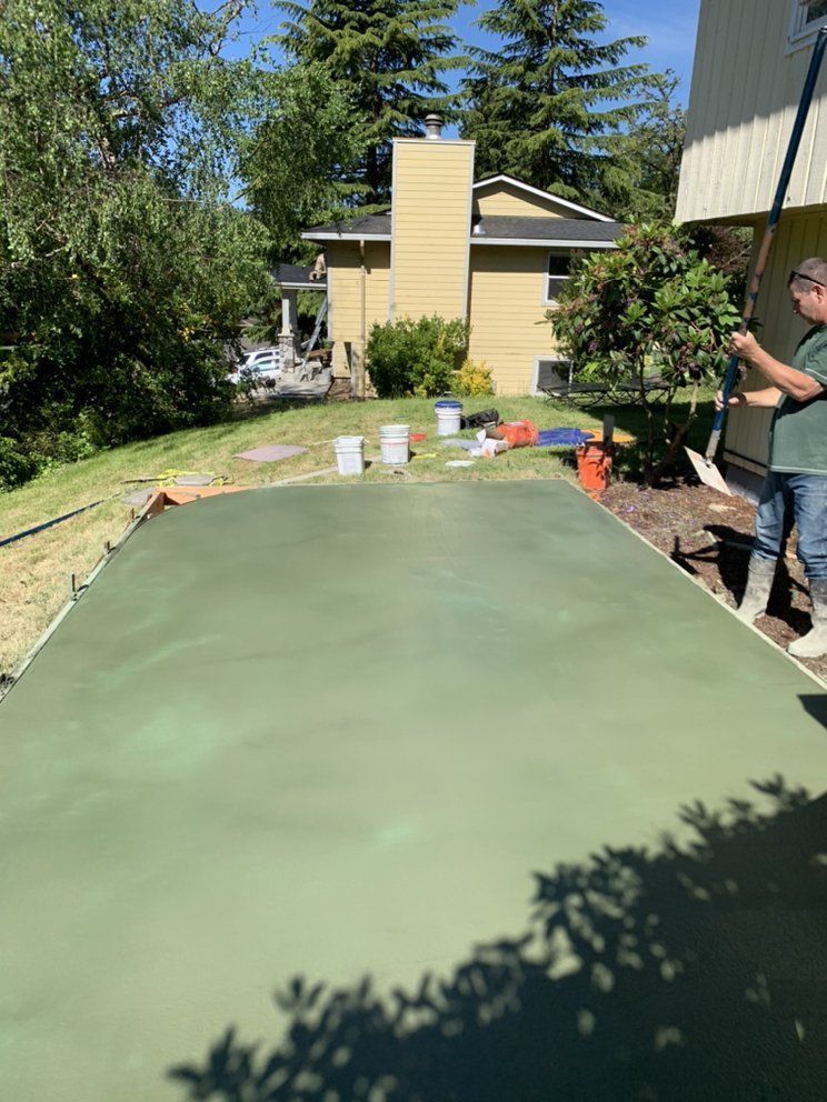 A man is standing on a green concrete driveway in front of a house.