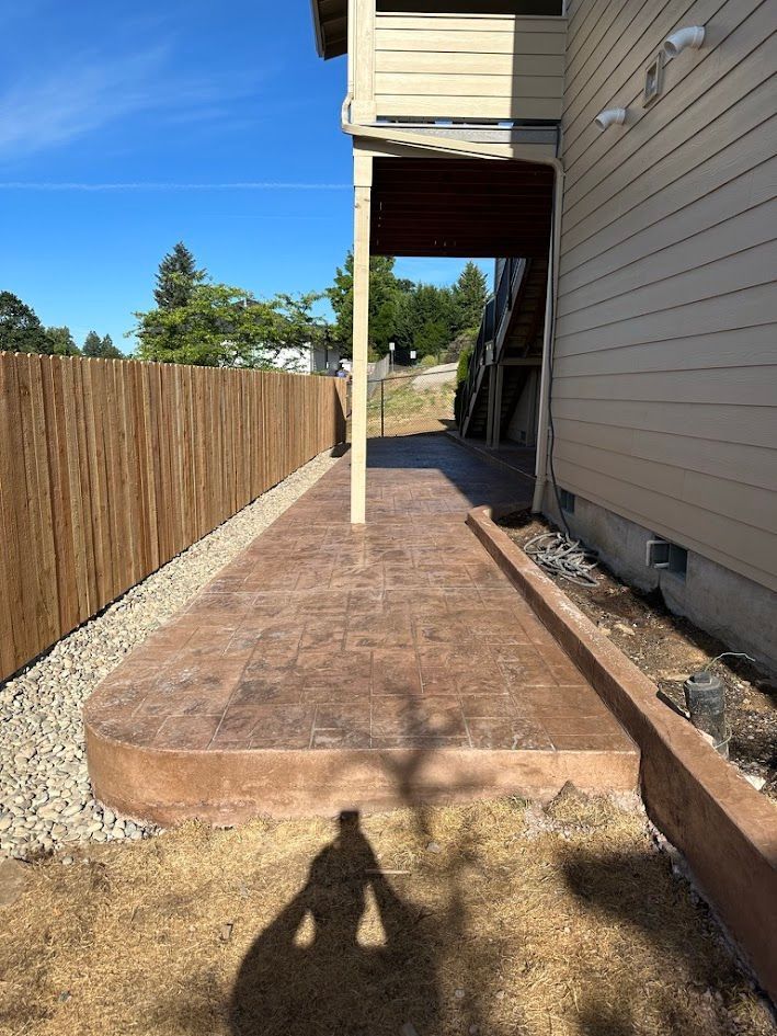 A concrete walkway leading to a house with a wooden fence.