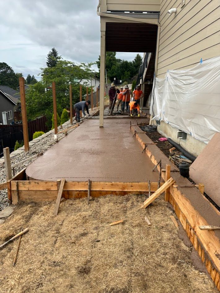 A group of construction workers are working on a concrete walkway in front of a house.