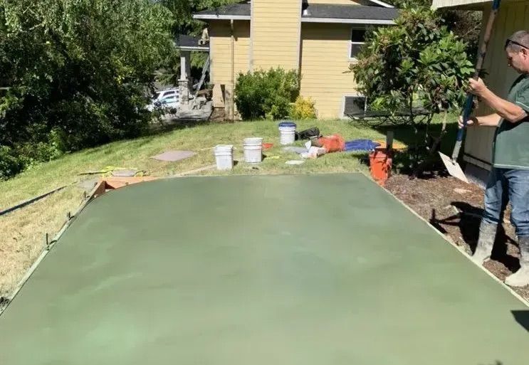 A man is standing on a green concrete surface holding a shovel.