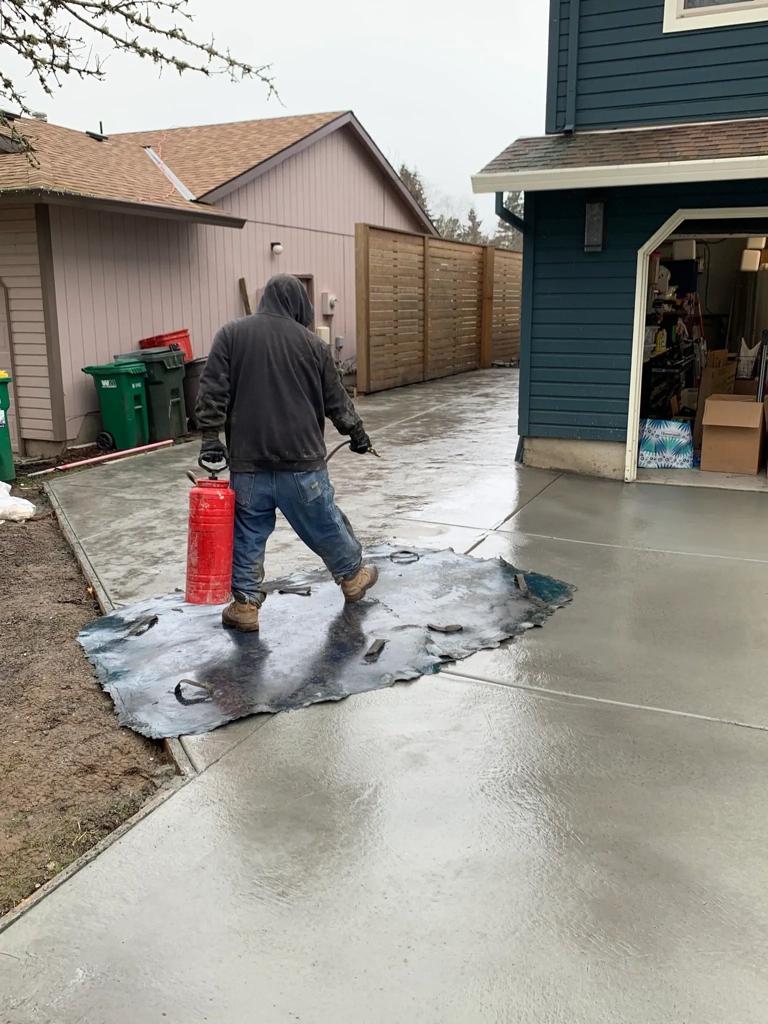 A man is spraying water on a concrete driveway in front of a house.