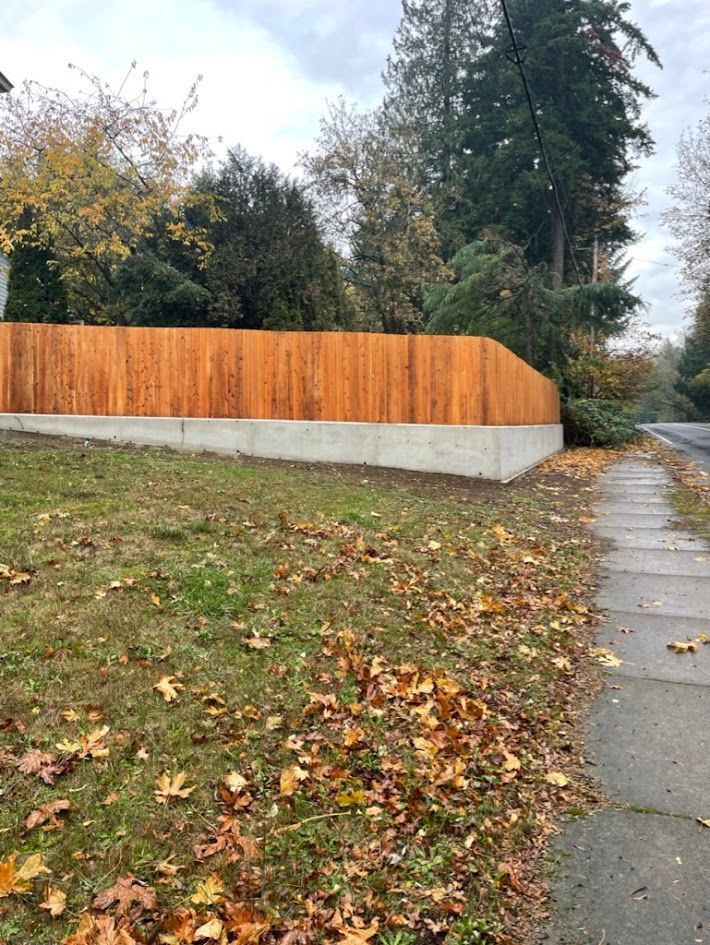 A wooden fence surrounds a grassy field next to a sidewalk.