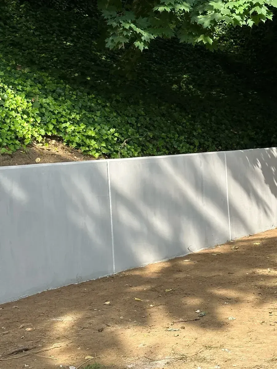 A white wall is surrounded by trees and dirt in a yard.