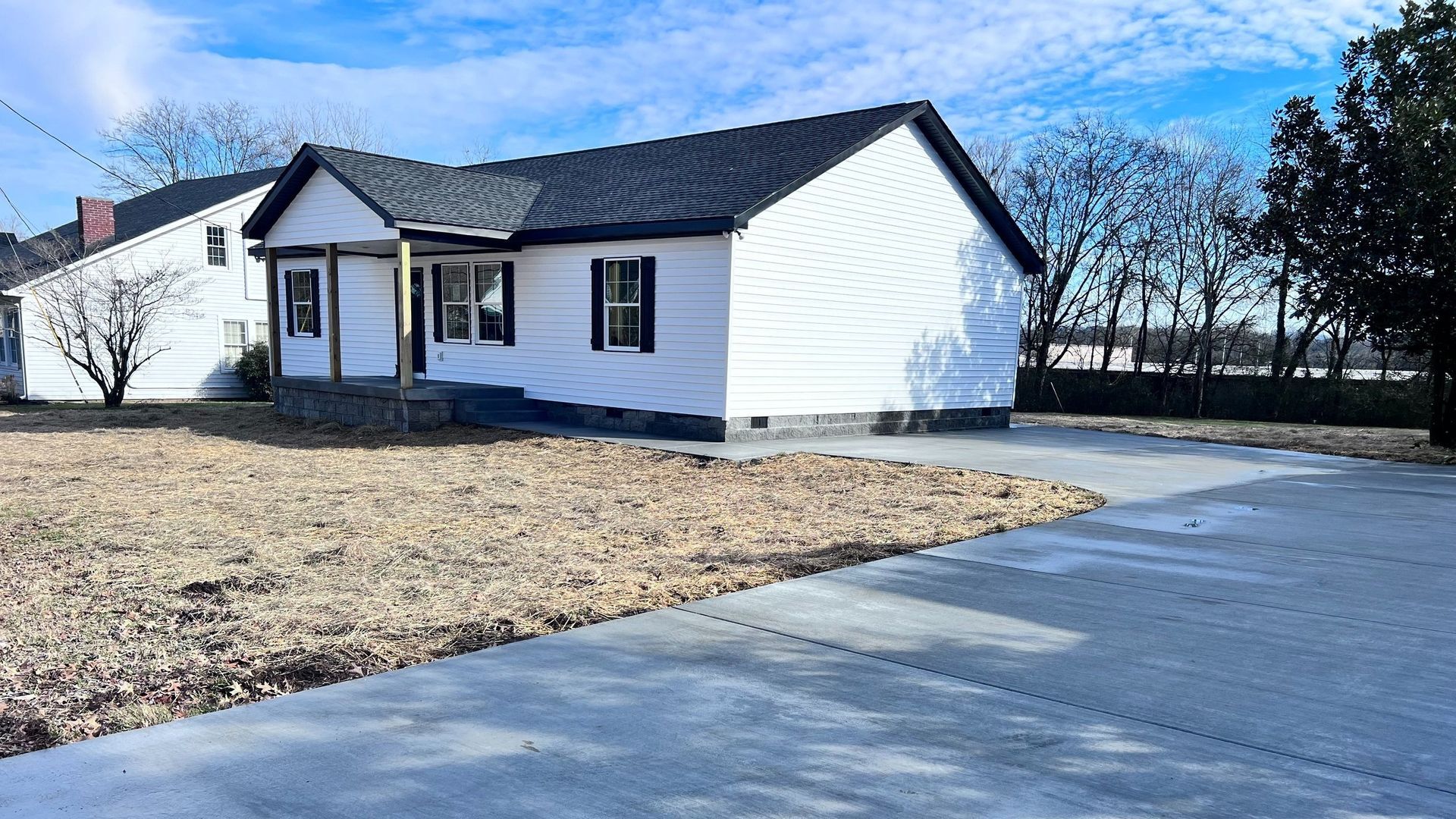 A white house with a black roof and a concrete driveway in front of it.