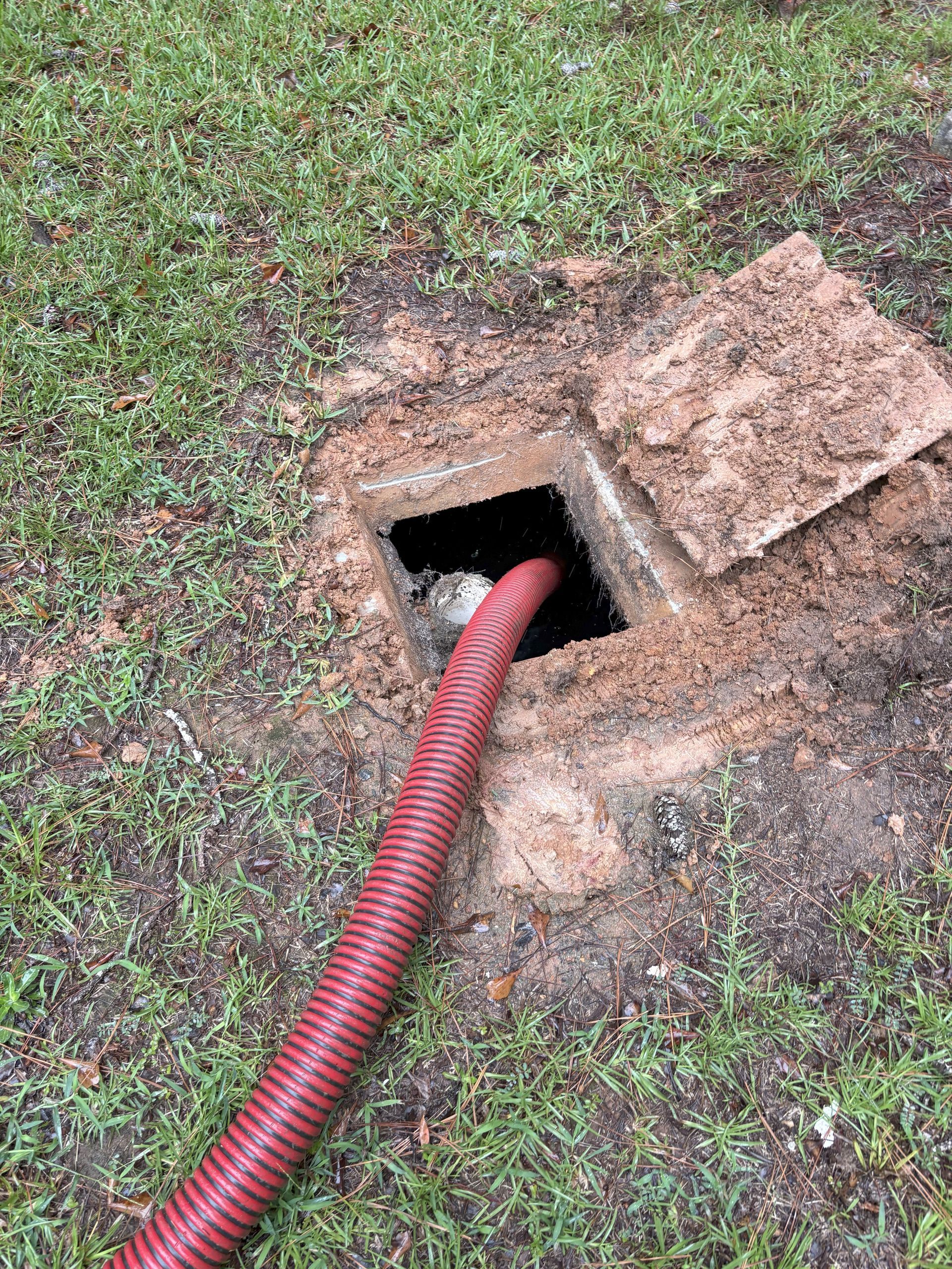Aerial view of construction site: trenches dug in a grassy field, next to a building.