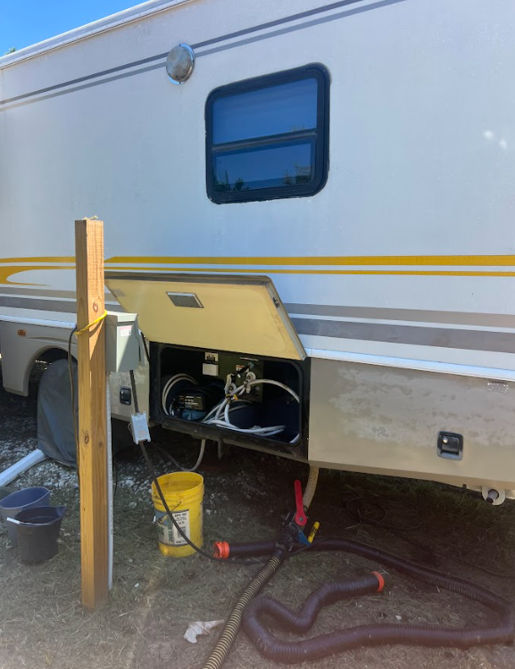 Man emptying RV waste tank using a hose outdoors.