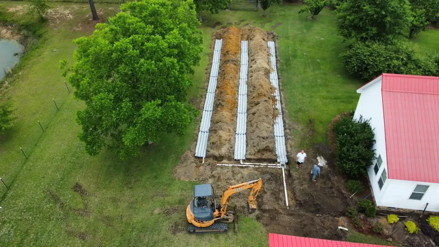 Aerial view of construction site with a small excavator and septic system installation near a house.