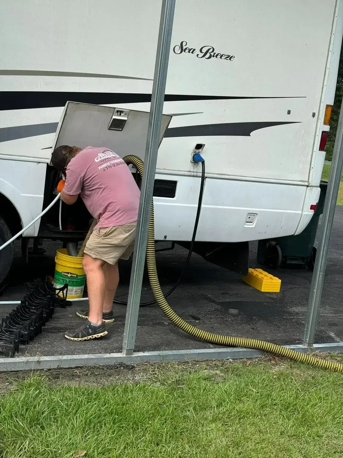 Man emptying RV waste tank using a hose outdoors.