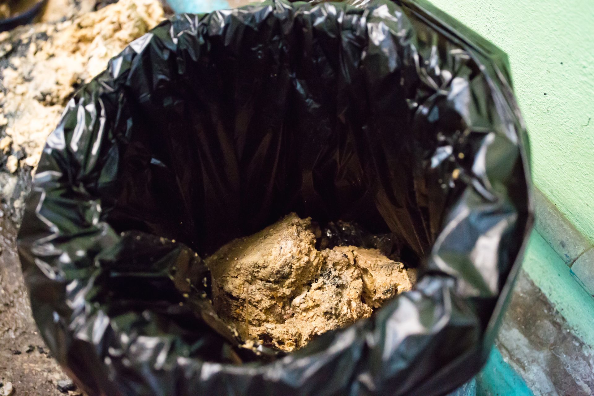 Black trash bag filled with tan-colored waste.