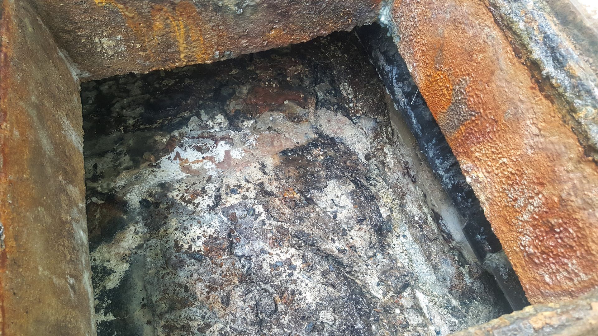 Rusting metal box with dark residue inside.