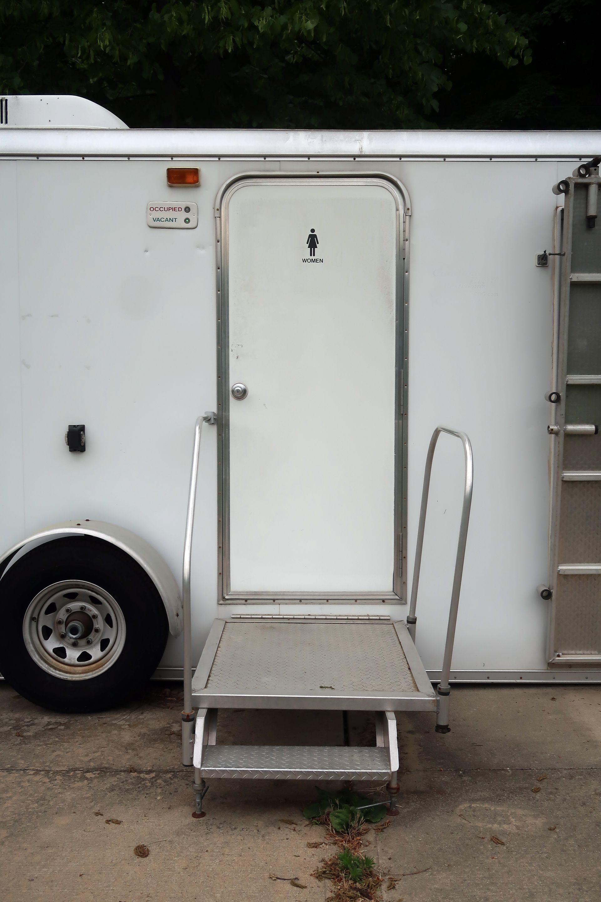 White trailer with a woman's restroom door and metal steps outside.