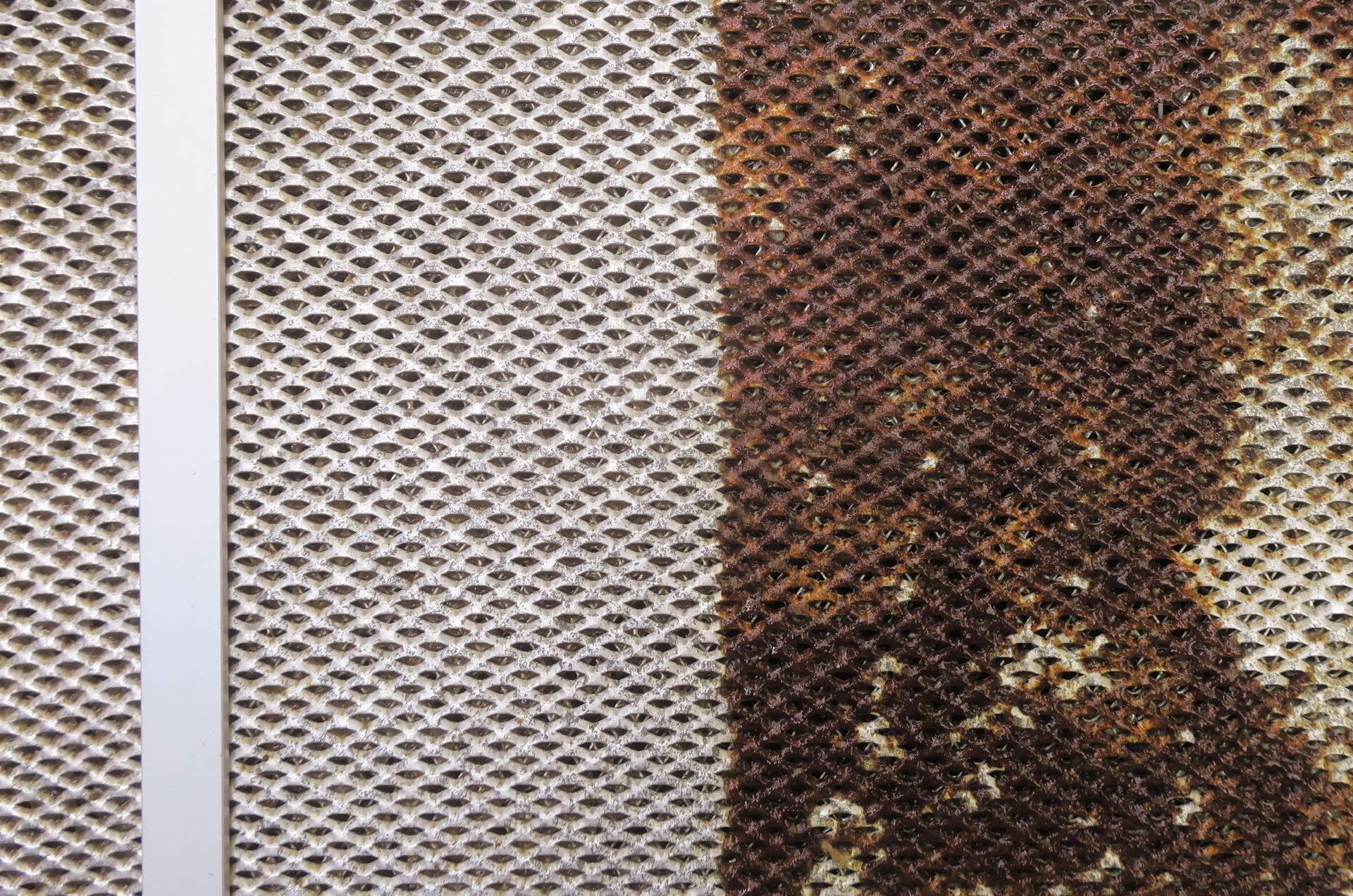 Close-up of a metal grate with heavy rust on the right side, a clean left side, and a vertical metal strip.