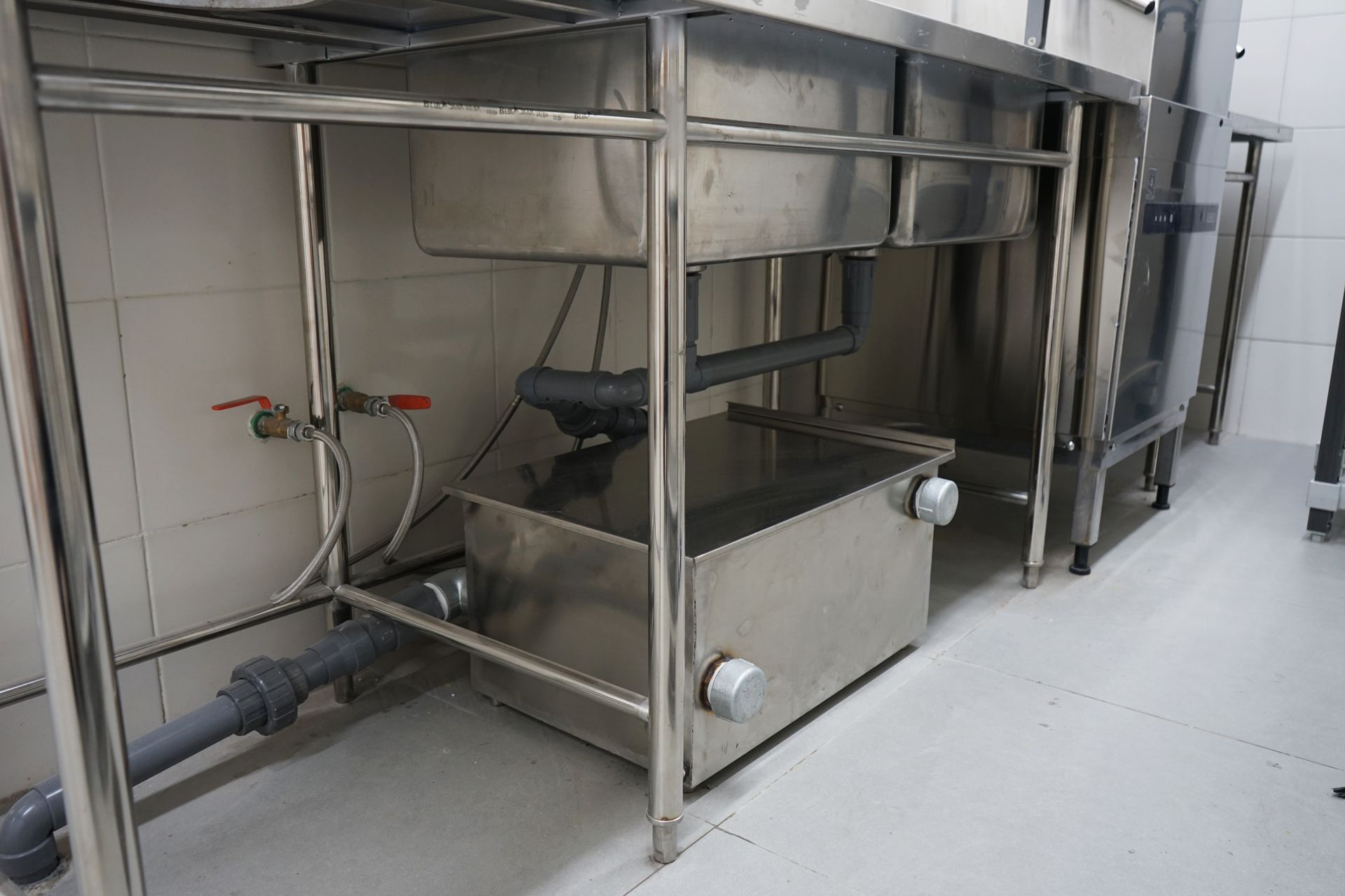 Stainless steel commercial kitchen sink with drain pipes and grease trap.