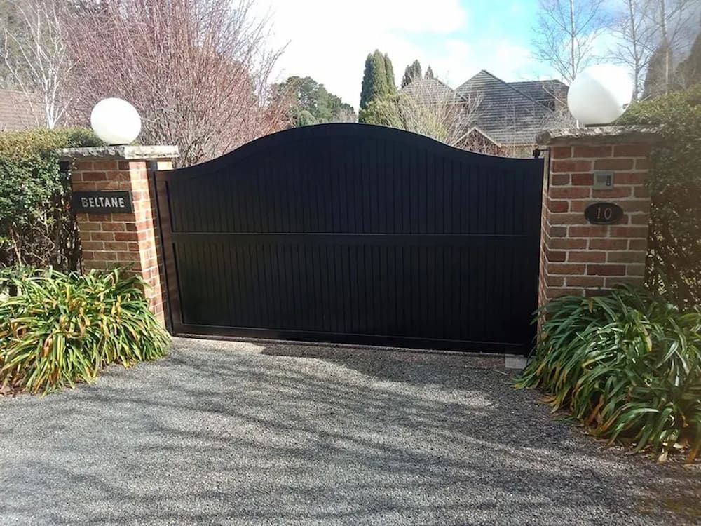 A Black Gate is Sitting in the Middle of a Driveway Next to a Brick Wall — Southern Gate Automation in Mittagong, NSW
