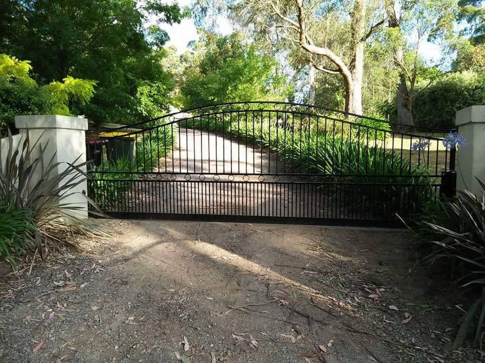 A Black Gate is Closed on a Dirt Road Surrounded by Trees — Southern Gate Automation in Picton, NSW