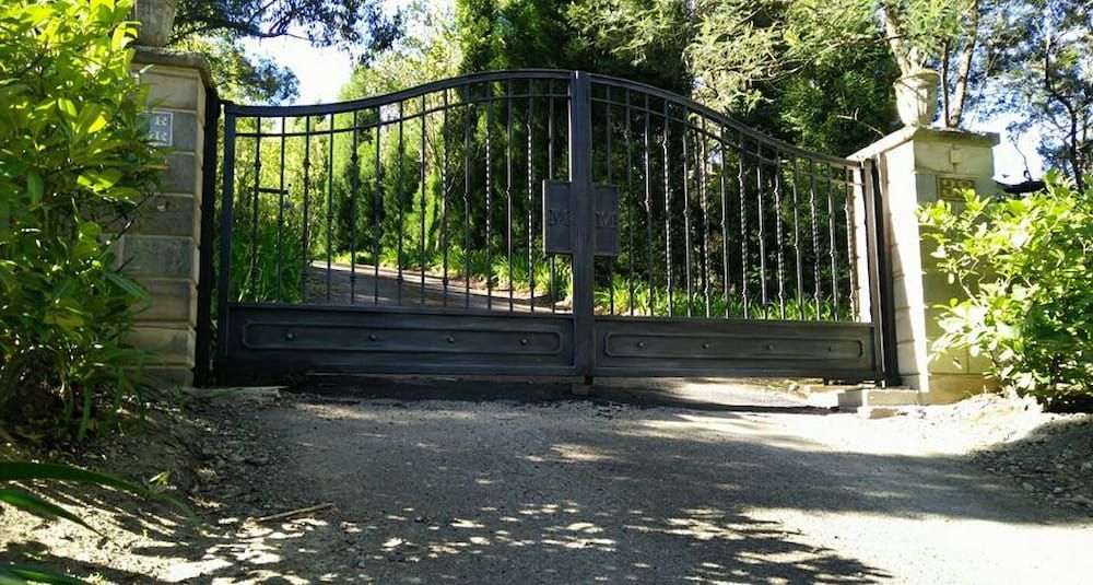 A Wrought Iron Gate is Sitting on the Side of a Dirt Road — Southern Gate Automation in Mittagong, NSW