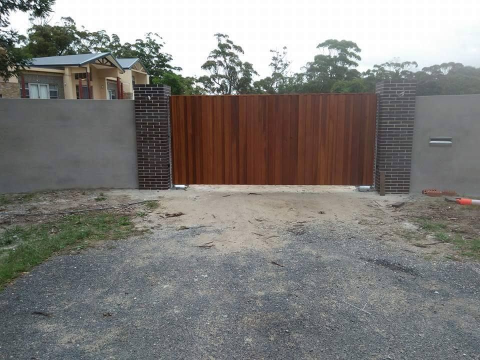 A Wooden Gate With a Brick Wall Behind It — Southern Gate Automation in Mittagong, NSW