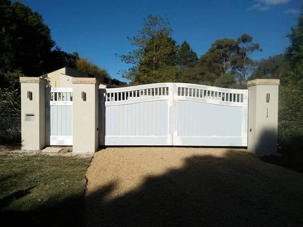 A White Gate is Surrounded by Concrete Pillars and a Gravel Driveway — Southern Gate Automation in Picton, NSW