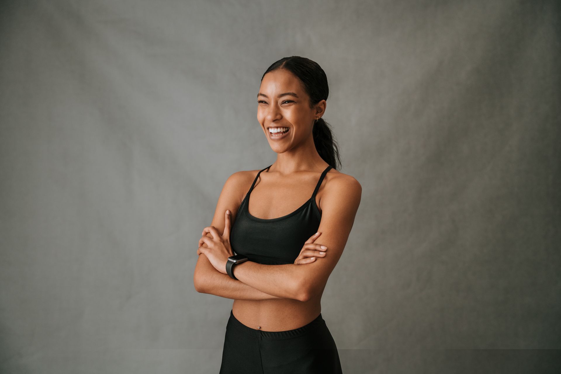 A woman in a black sports bra is standing with her arms crossed and smiling.