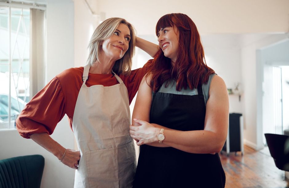 Two women in aprons are standing next to each other in a salon.
