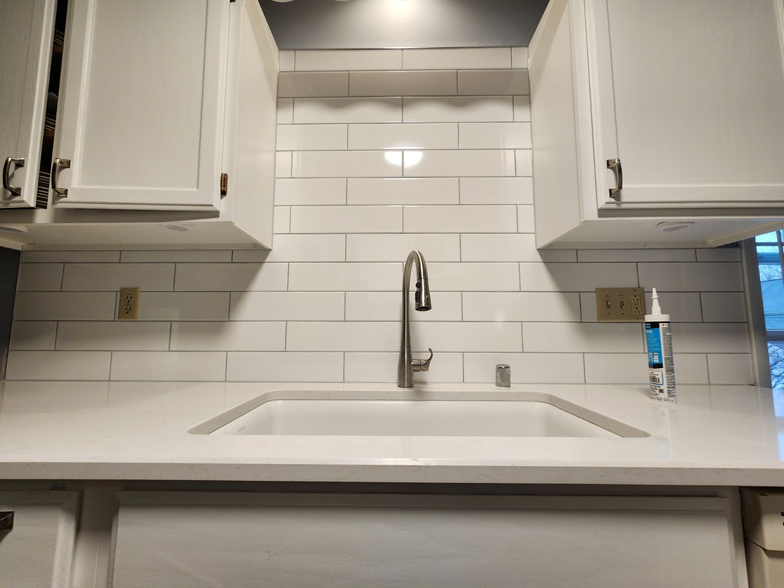White kitchen with subway tile backsplash and stainless steel faucet.