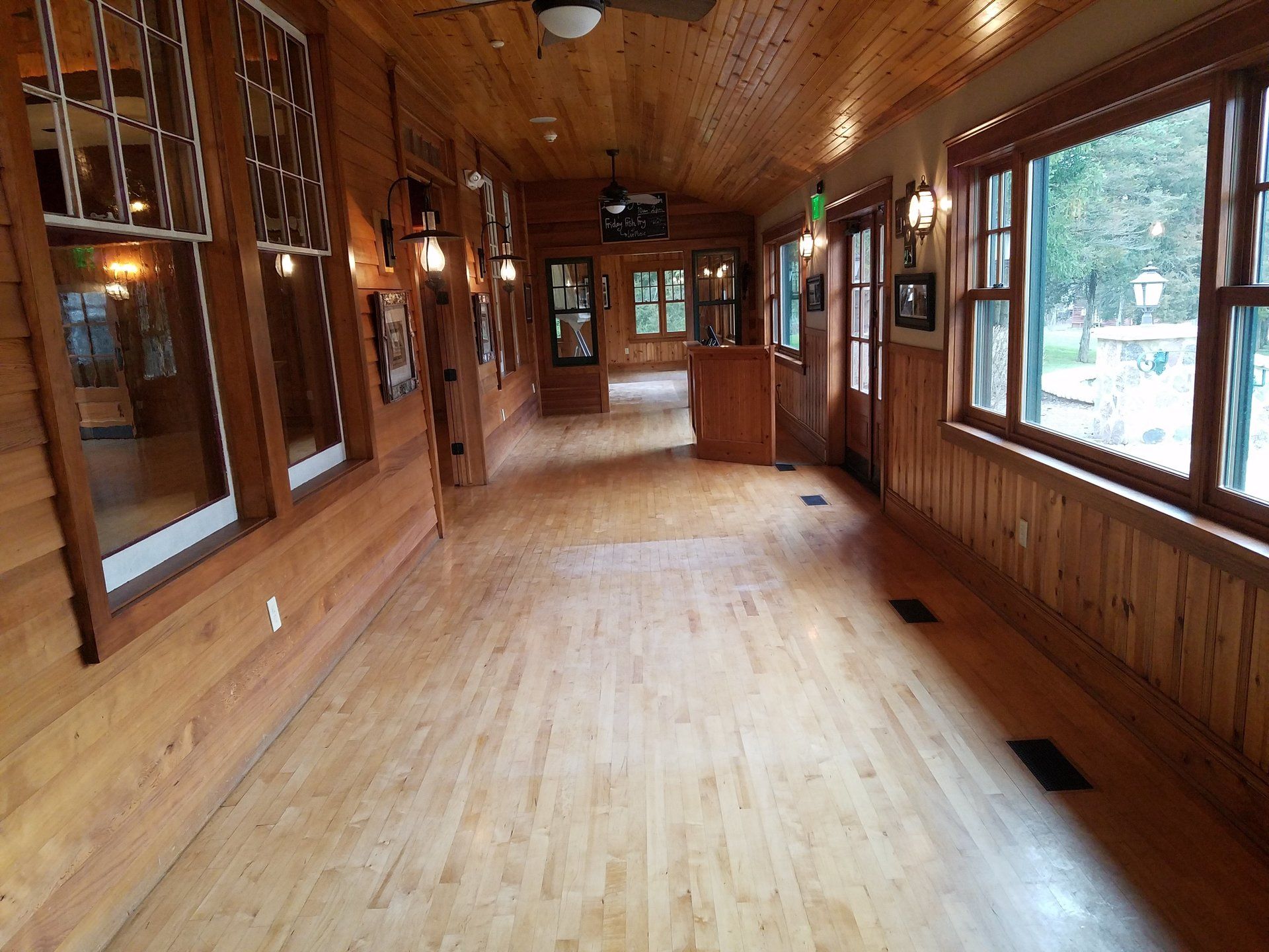 Long wooden hallway with windows, doors, and light fixtures.