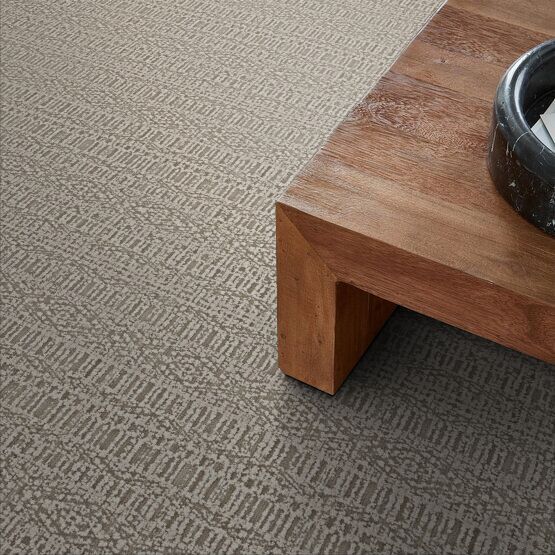 Tan patterned carpet beside a wooden coffee table with a decorative bowl on top.