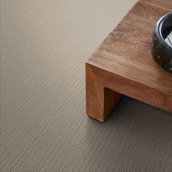 Beige carpet with a corner of a brown wooden coffee table.