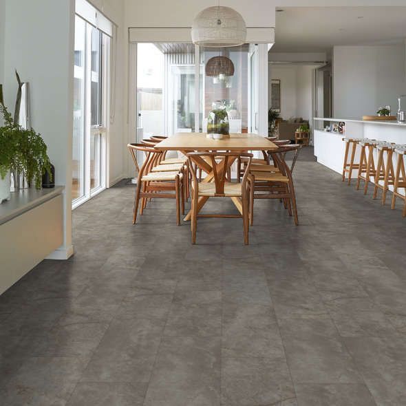 Dining room with gray tile floor, wooden table & chairs. Kitchen with white counter & bar stools visible.