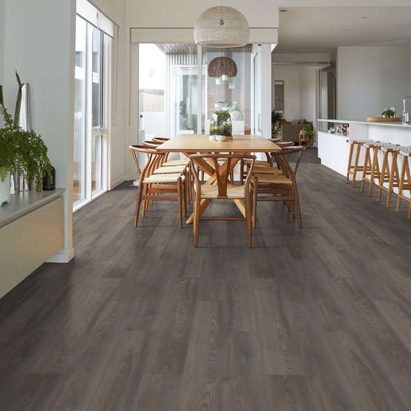 Dining room with gray wood-look flooring, wooden table and chairs, and a white kitchen in the background.